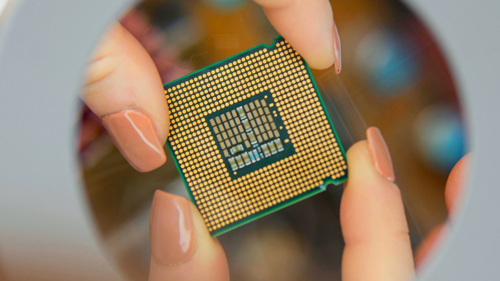 A woman holding an intel microprocessor and inspecting it through a lens