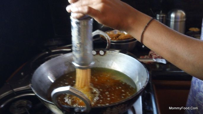 Pressing dough through chakrala gidda into hot oil for frying