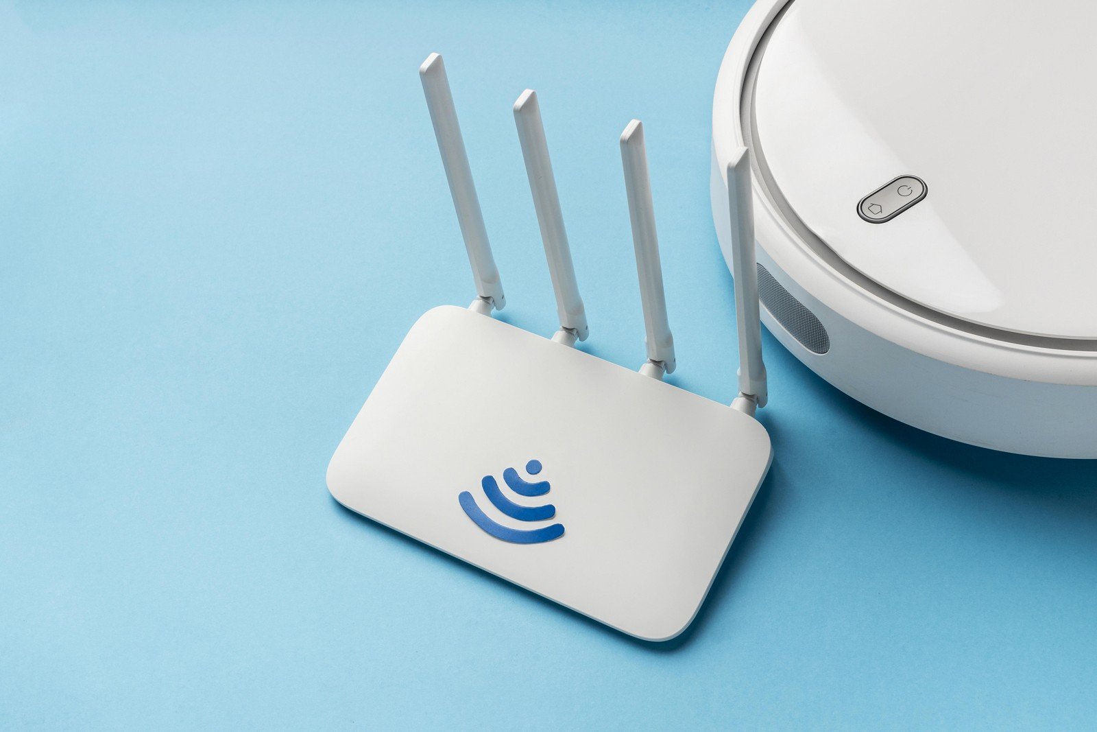 A wireless router with four antennas and a Wi-Fi logo, placed on a light blue surface next to a smart device.