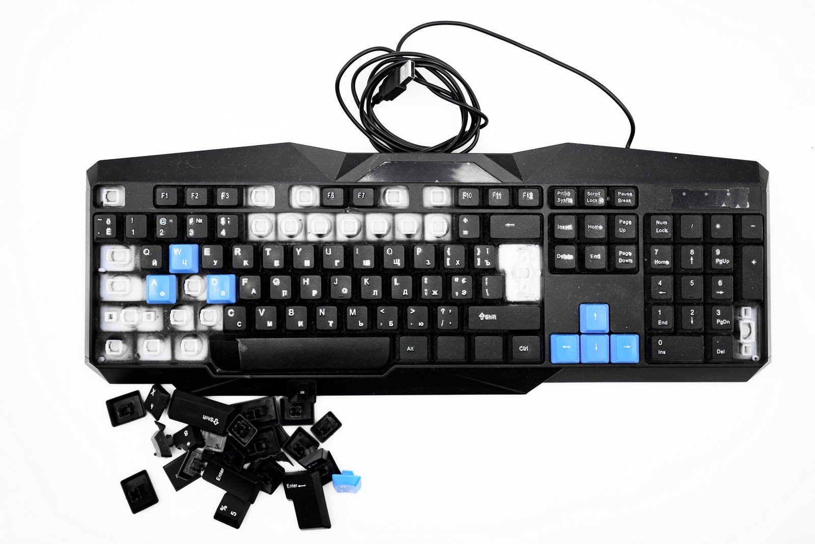 A disassembled membrane keyboard showing detached keycaps, blue directional keys, and a visible circuit layout beneath, highlighting its construction and design.