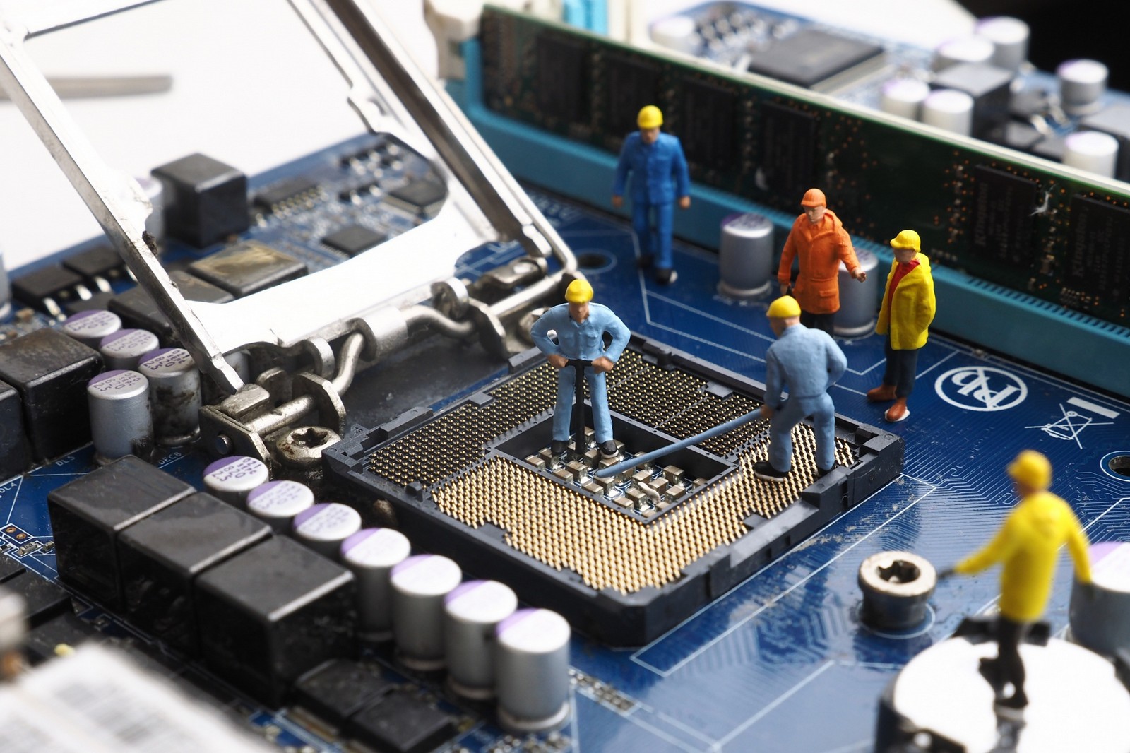 A close-up image of miniature figurines resembling workers inspecting and "building" a CPU socket on a computer motherboard, illustrating the intricate nature of computer hardware components.